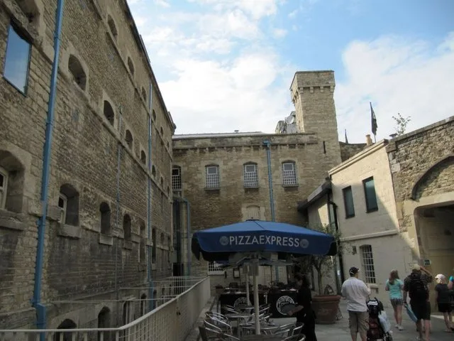 The Pizza Express terrace in the Oxford Castle Quarter courtyard in 2009, with blue parasols below the stone walls of the old prison and the castle tower