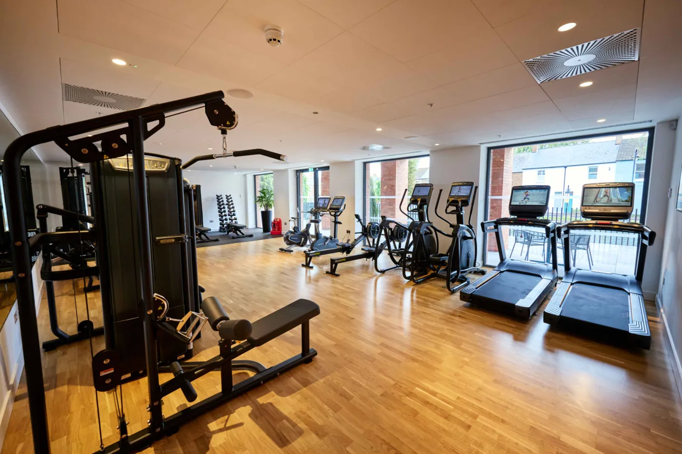 A gym with weights machines, treadmills and cross trainers by large windows