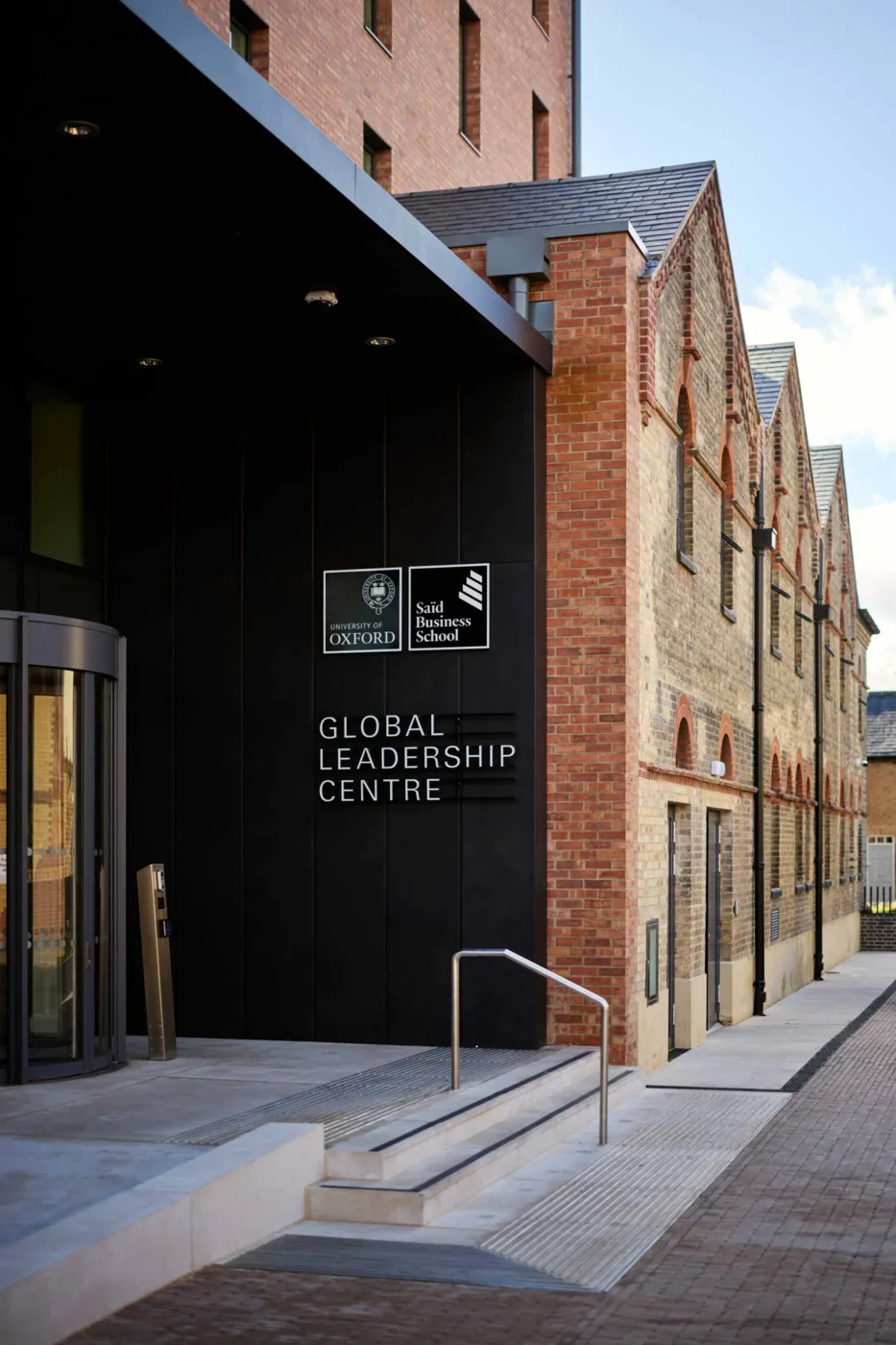 The front entrance of the Global Leadership Centre, a dark clad doorway with the centre's name beside it and the brick gable of the old building above