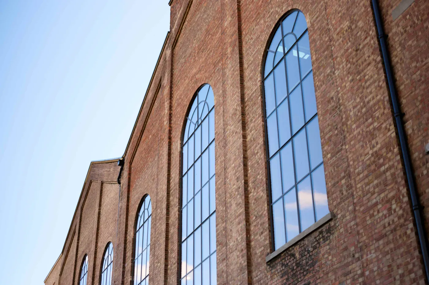 Tall arched windows set in the old brick wall of the power station, seen from below against a blue sky