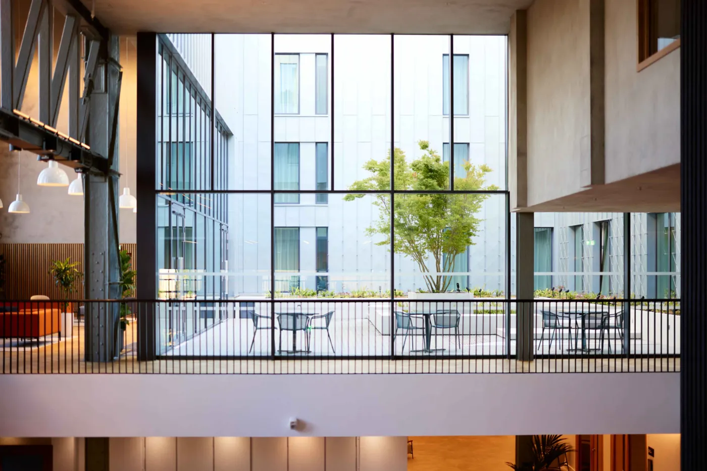 An inner courtyard with tables and a tree, seen through tall glass from a balcony
