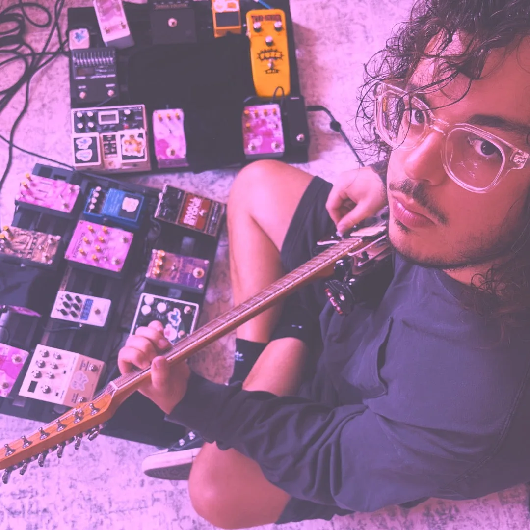 Luca of violet oscillation sitting with an electric guitar beside rows of guitar effects pedals on the floor